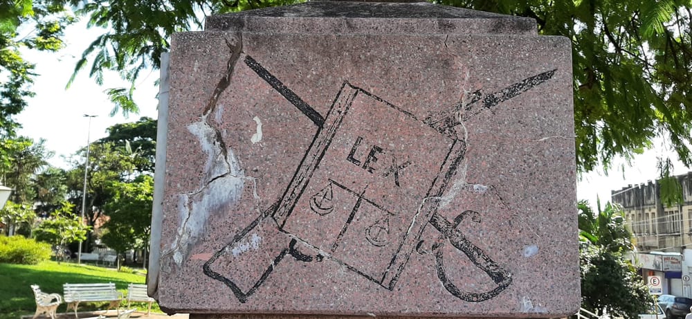 Relevo na base do monumento, com o livro da lei marcado "LEX", a balança, a espada e o fuzil cruzados.